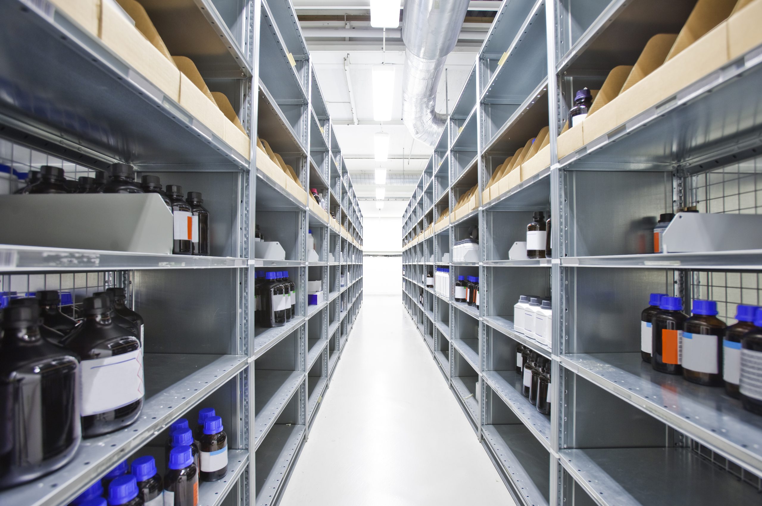 Neatly organized chemical storage with rows of labeled chemical bottles on metal shelving in a clean, well-lit facility.